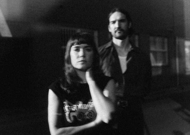 Black and white portrait of noise rock duo Party Dozen with saxophonist Kirsty Tickle in front and drummer Jonathan Boulet behind.